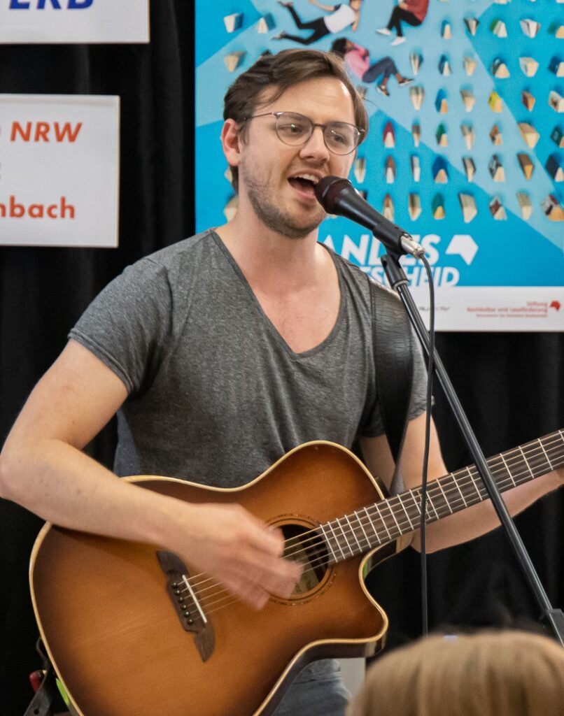 Basti Smolka mit Gitarre singend vor einem Mikrofon stehen.
