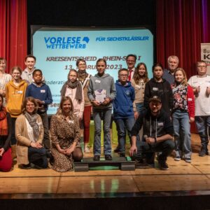 16 Kinder stehen gemeinsam als Gruppe auf der Bühne des Rheinbacher Stadttheaters und lachen in die Kamera.