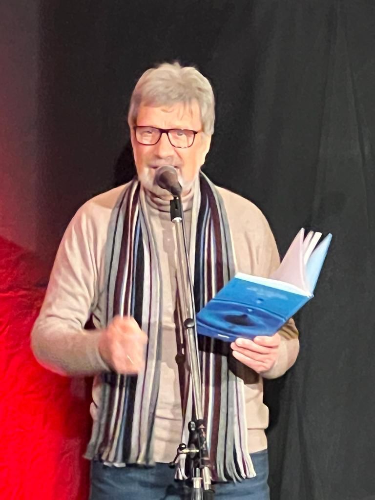 Günter Detro mit aufgeschlagenem Buch am Mikrofon.