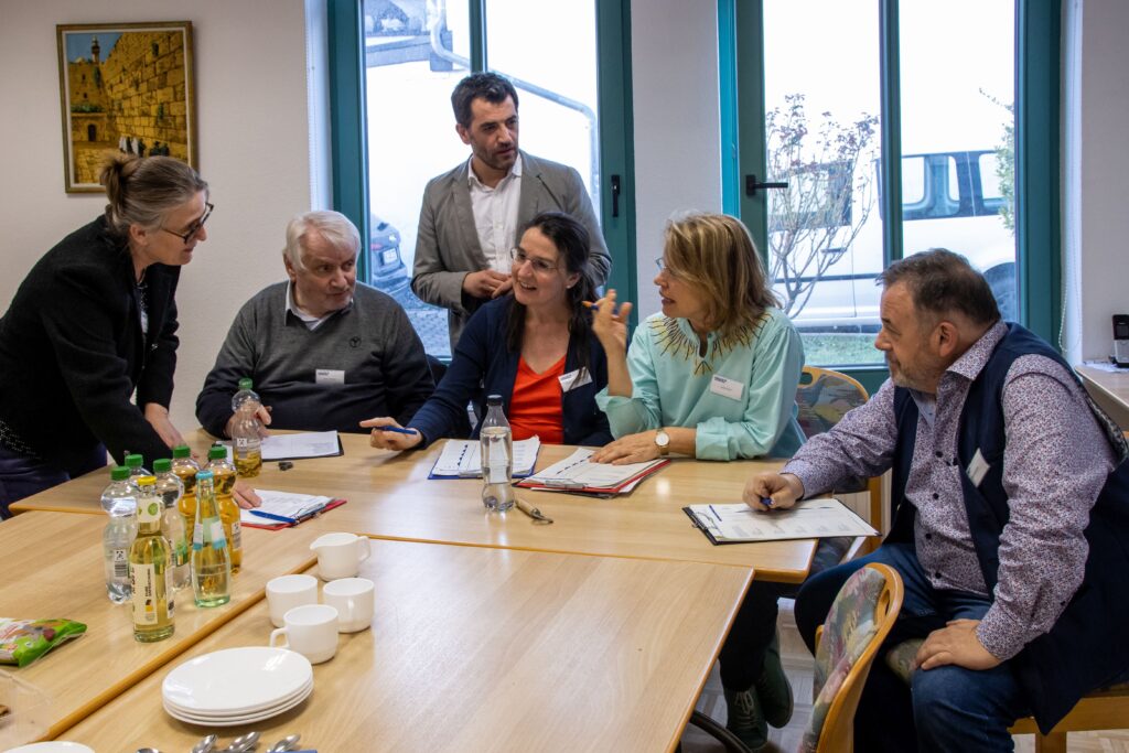 Die gesamte Jury aus dem ganzen Regierungsbezirk sitzend an einem Tisch in einem intensiven Gespräch.
