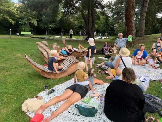 Gruppe von Kindern sitzend und liegend auf der Wiese und hören gebannt dem Vorleser zu.