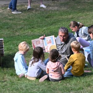 Ehrenamtlicher Vorleser in einer Gruppe interessierter Kinder auf der Wiese sitzend.