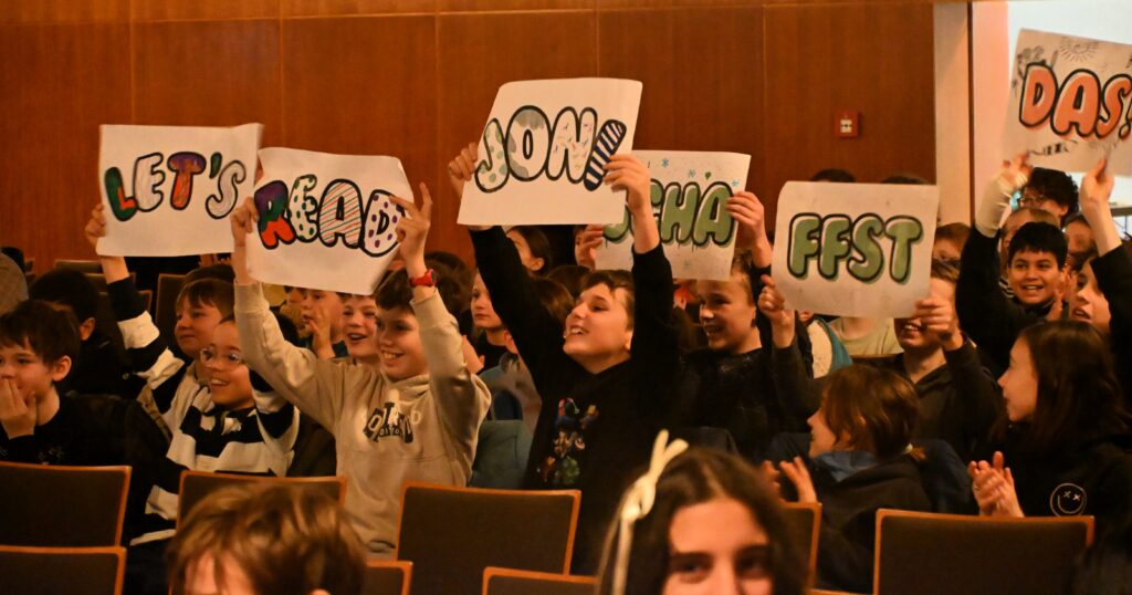 Zahlrreiche Schüler*innen feuern die Vorleser*innen mit bunten Plakaten an.