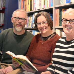 Martin Groß, Christel Engeland und Martina Münch sitzend vor einer schönen Bücherwand und strahlend lachend.